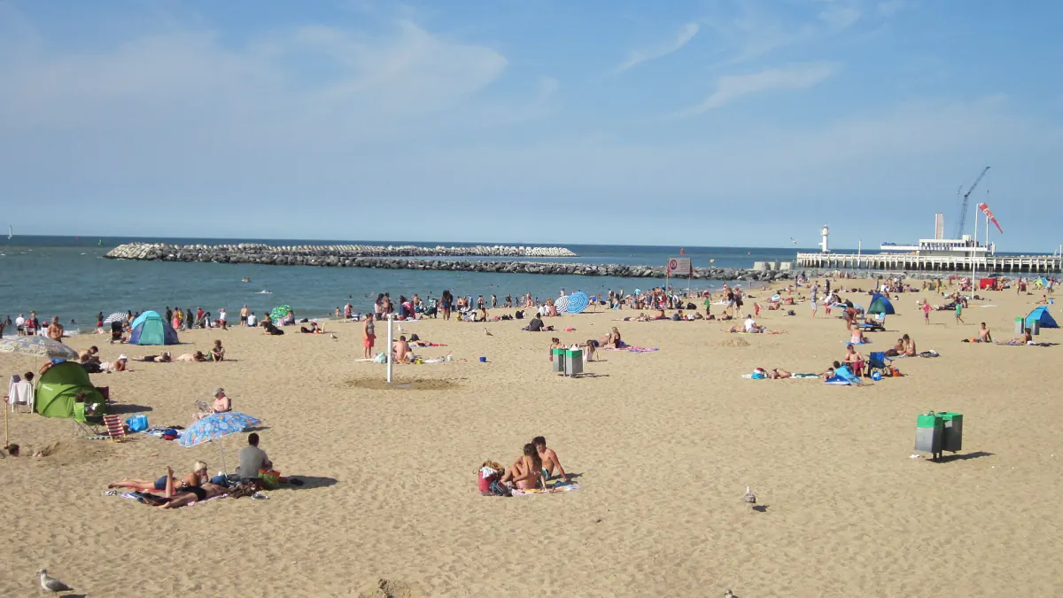 Plage animée d'Ostende un jour ensoleillé, avec les estacades et un ferry au loin