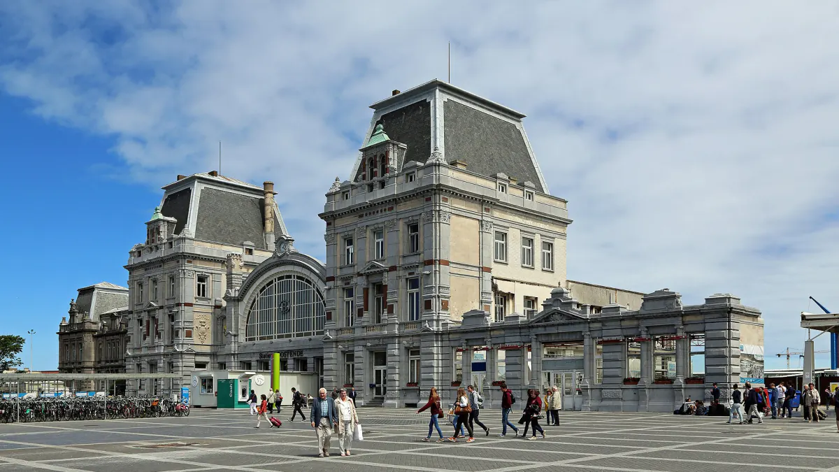 Façade de la gare d'Ostende vue depuis la place, avec des voyageurs qui traversent