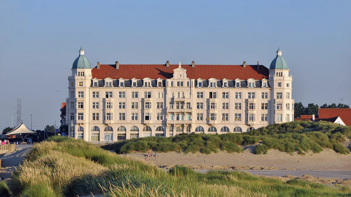 Grand bâtiment à toit rouge et tourelles, derrière les dunes à Zeebruges